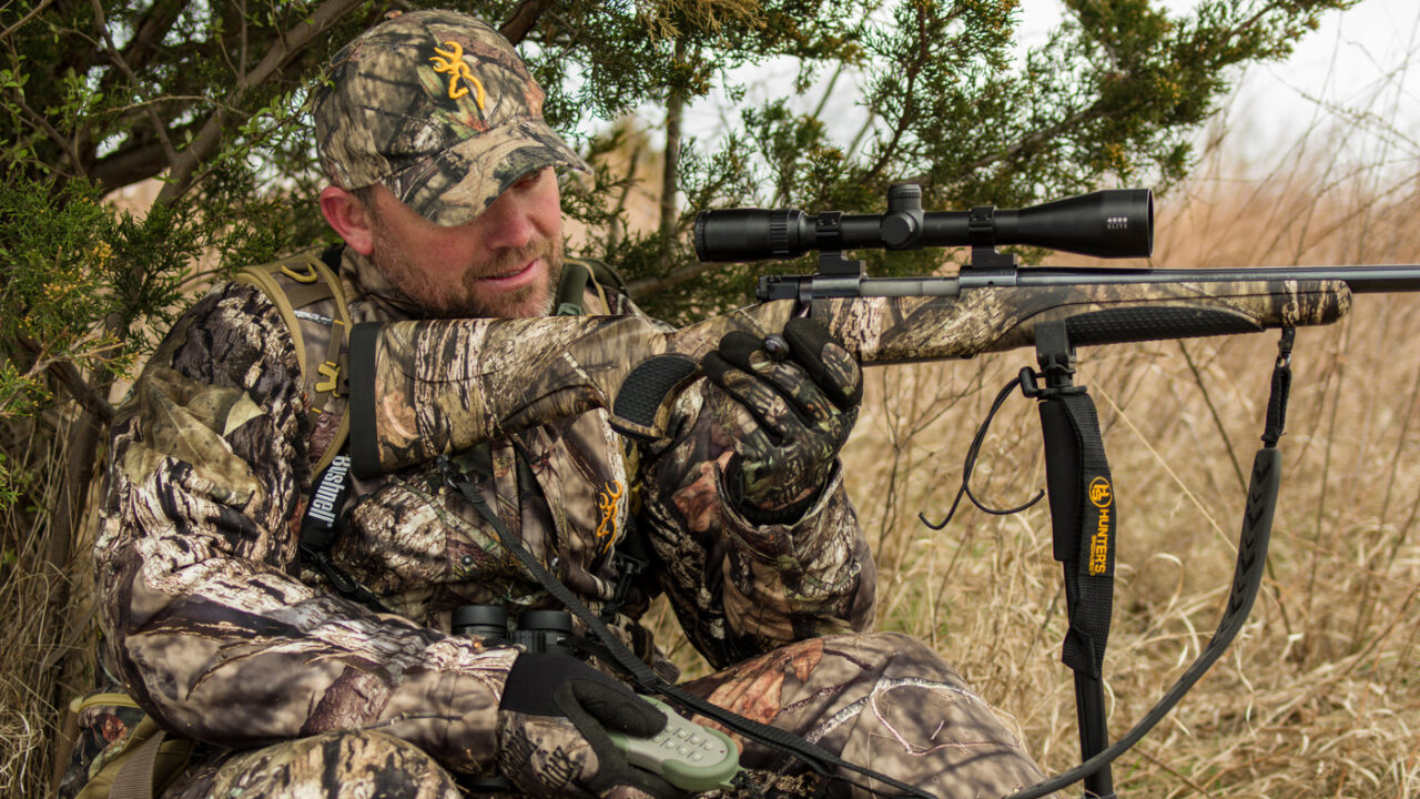 camouflaged predator hunter shooting a rifle off a rest