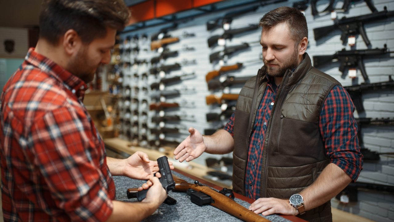 A gun store owner shows a customer a handgun
