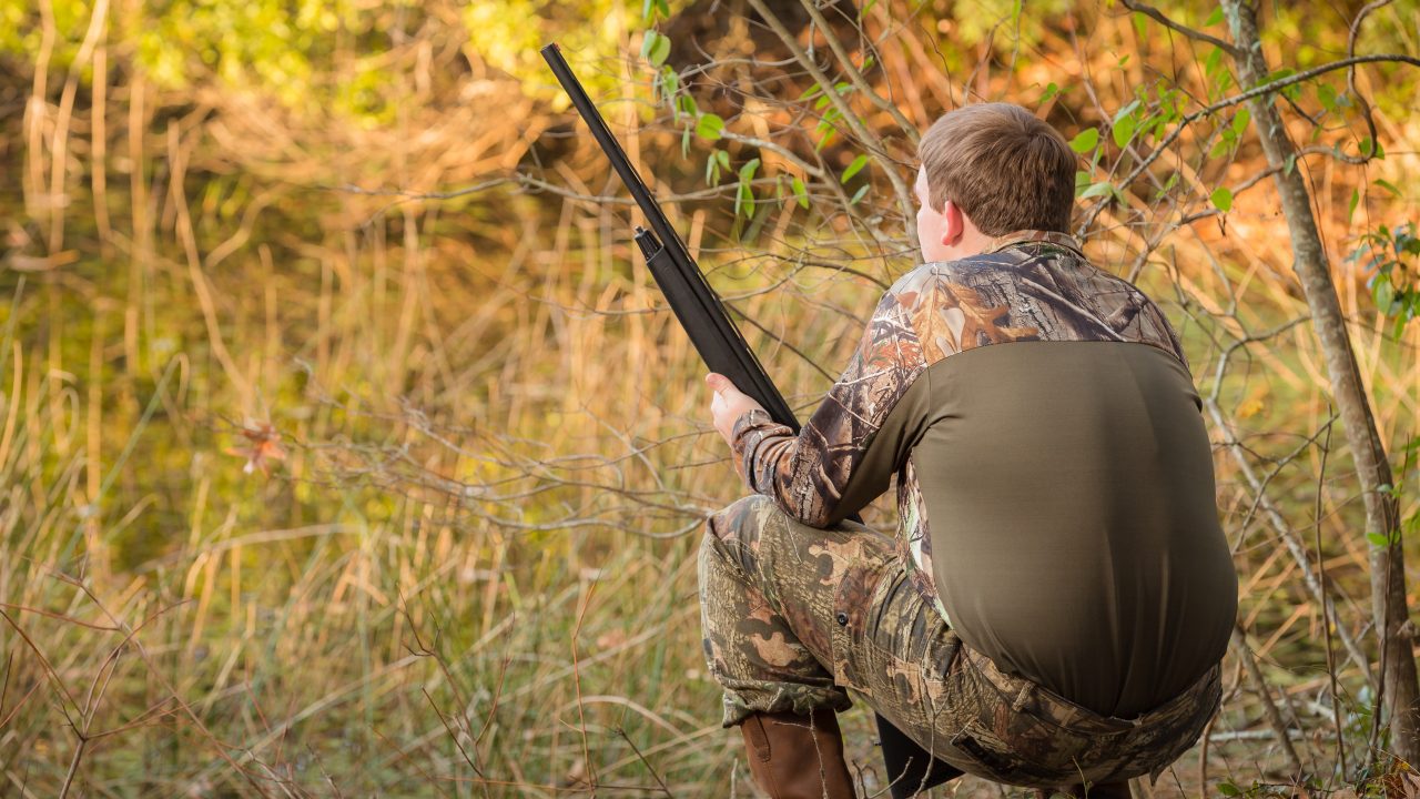 Teenage boy hunting with gun pond and camouflage