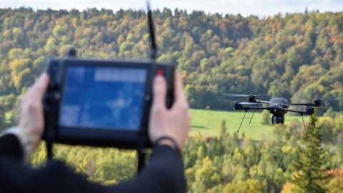 black flying drone in sky with handler looking at screen to locate wounded game after hunting